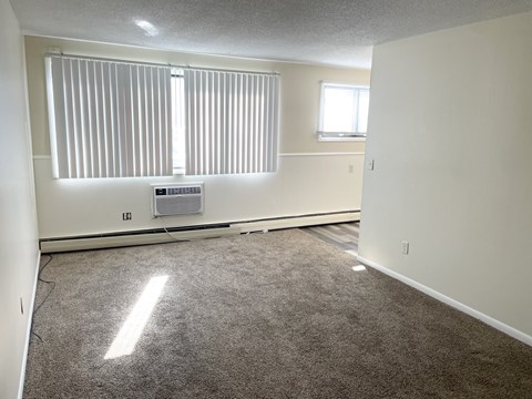 A room with a window covered by blinds and a small air conditioning unit on the wall.